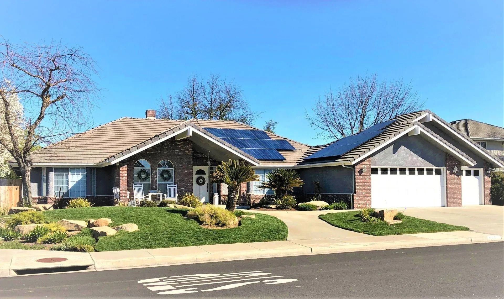 Single-story house with solar panels on the roof, blue sky, green lawn, and a driveway.