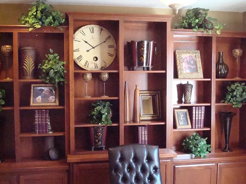 Wooden built-in bookshelves with various decorative items, including a large clock and greenery.