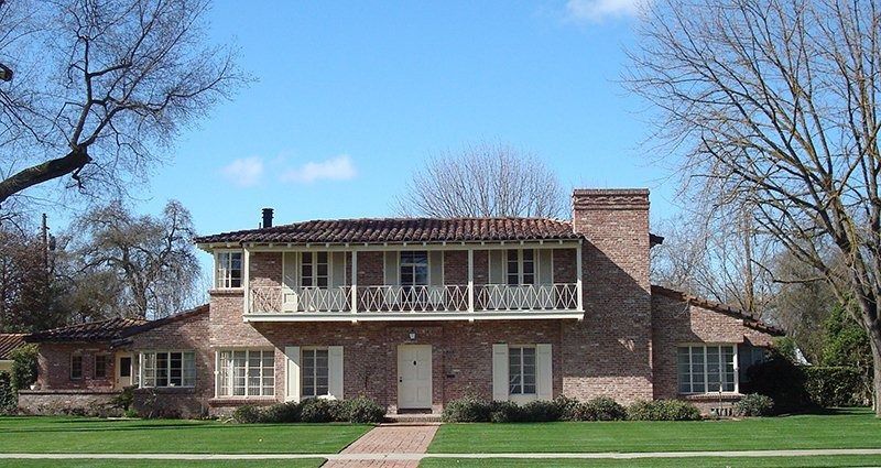 Brick house with balcony, red tile roof, and green lawn under a blue sky.