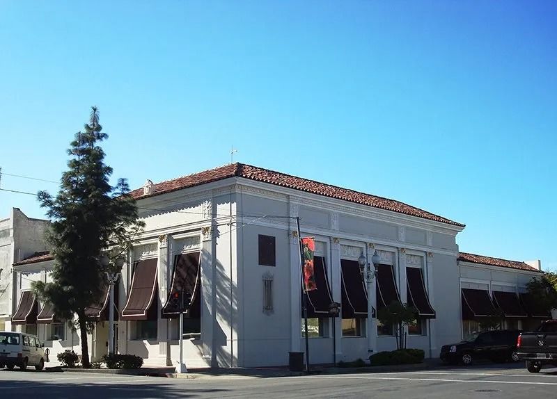 Cream-colored, two-story building with brown awnings. A few vehicles parked on the street in front under a clear blue sky.