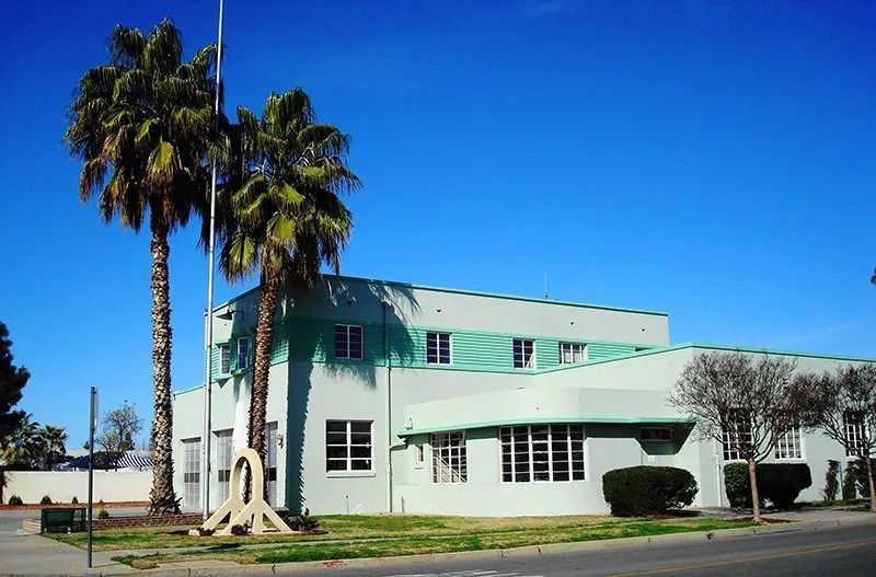 Light green Art Deco building with palm trees against a blue sky.