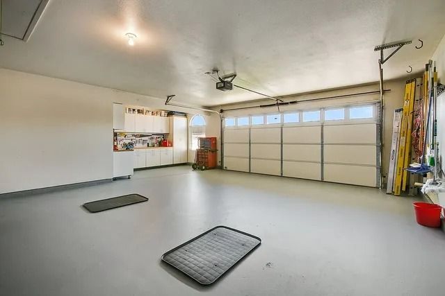 Empty, clean garage with gray floor, white walls, and closed garage door. Two mats on the floor.