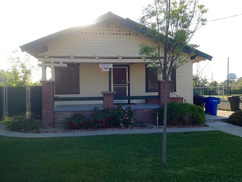 Yellow Craftsman style house with porch and brick columns, set on a green lawn.