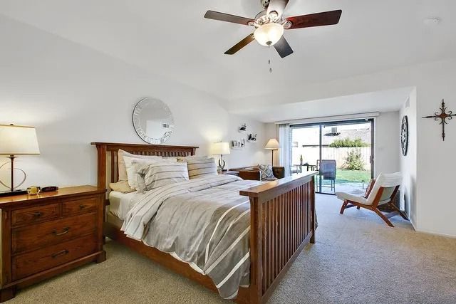 Bedroom with wooden bed, dresser, and sliding door to patio. Beige carpet and white walls.