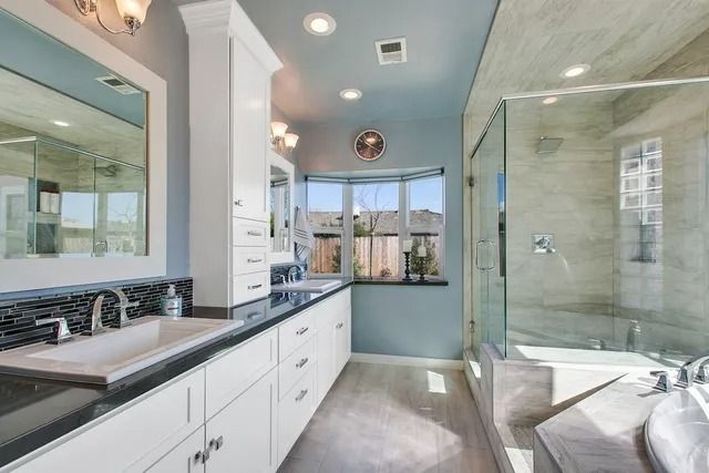 Spacious bathroom with white cabinets, dark countertops, blue walls, a large mirror, and glass shower.
