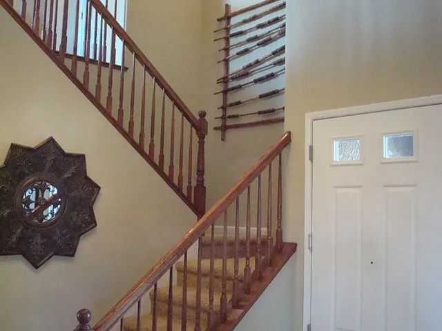 Staircase with wooden railing, a front door, and a decorative sunburst mirror on the wall.