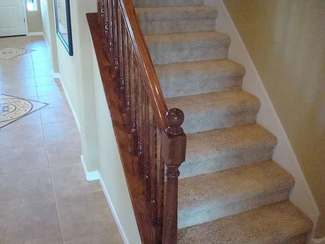 Staircase with carpeted steps and wooden railing in a home, beige walls.