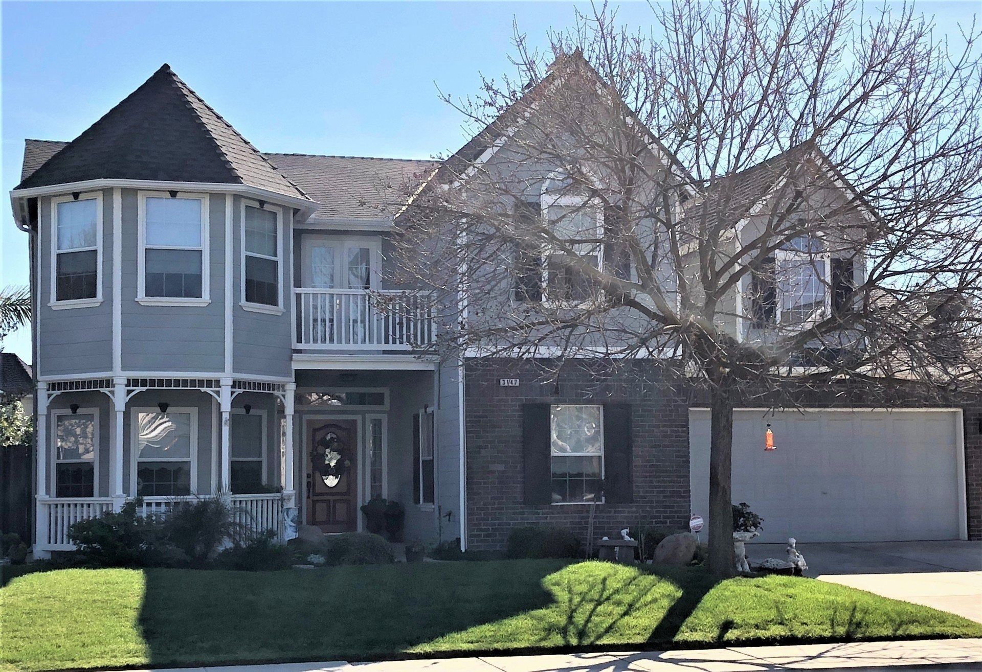Two-story house with light blue siding, gray roof, balcony, and detached garage.