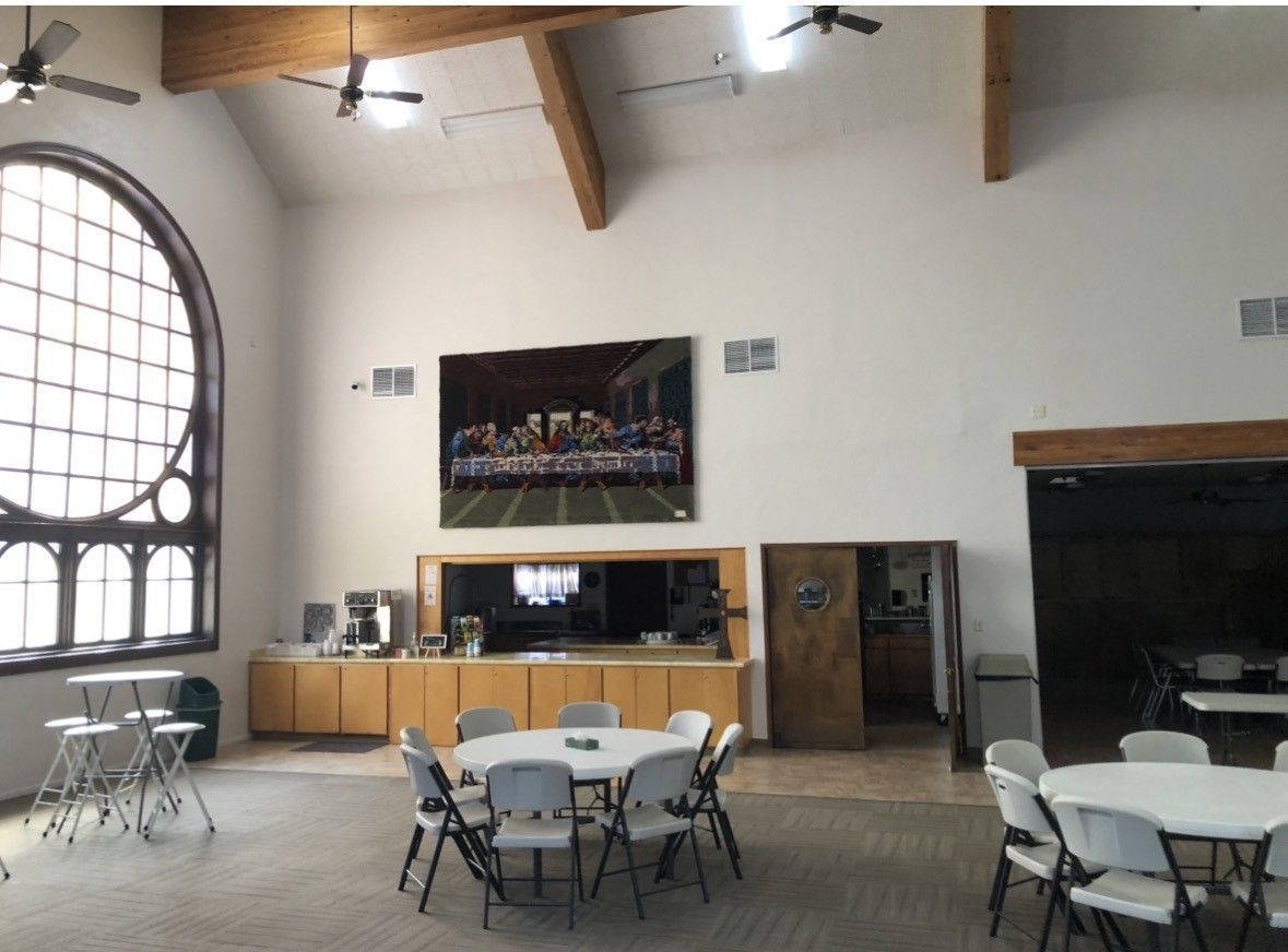 Interior of a room with tall arched window, tables, chairs, coffee station, and a Last Supper painting.