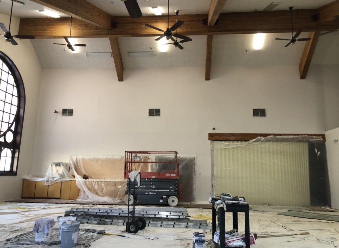 Interior room under construction with exposed beams, stained glass window, and equipment.