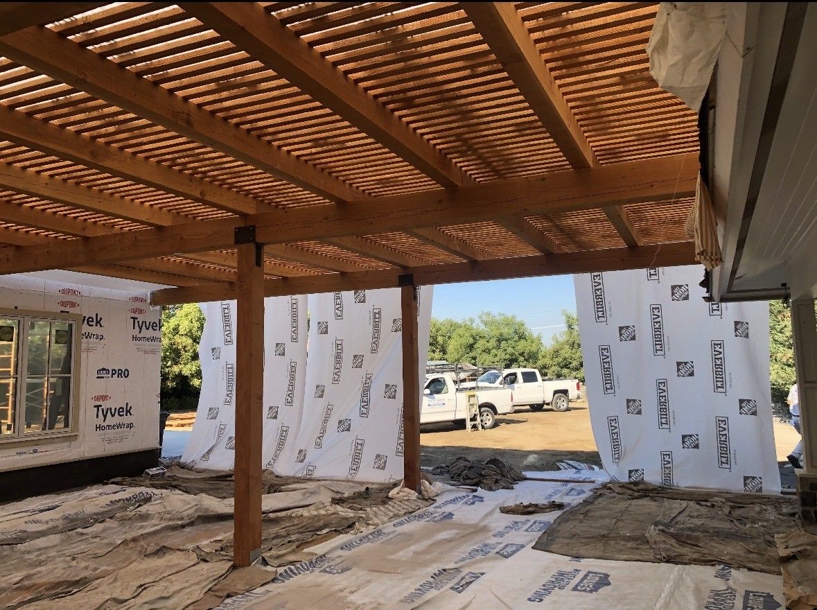 Wooden pergola under construction, attached to a house. Construction materials are visible.