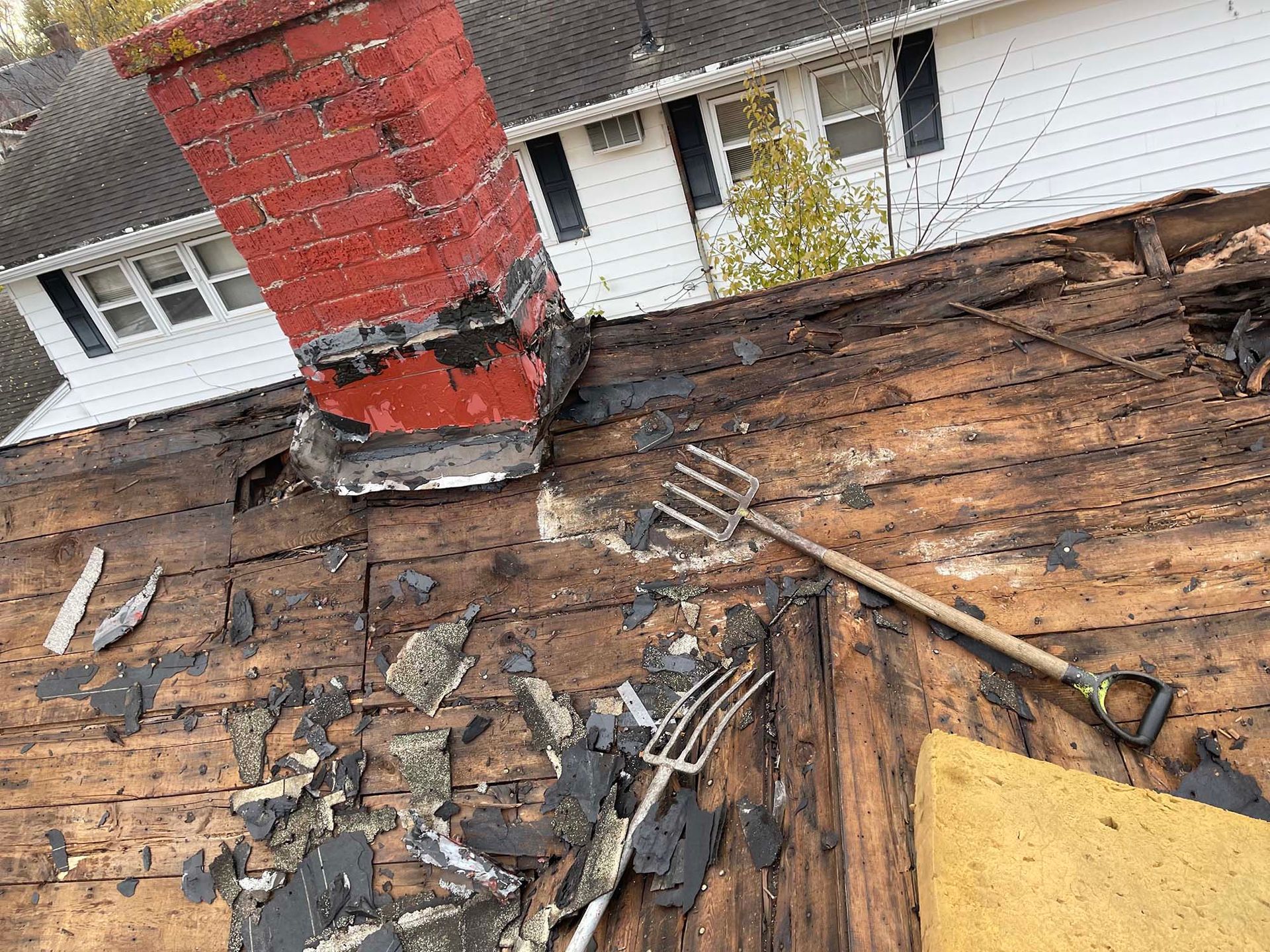 Rotted roof with a damaged red brick chimney, and a garden fork resting on the wooden planks.