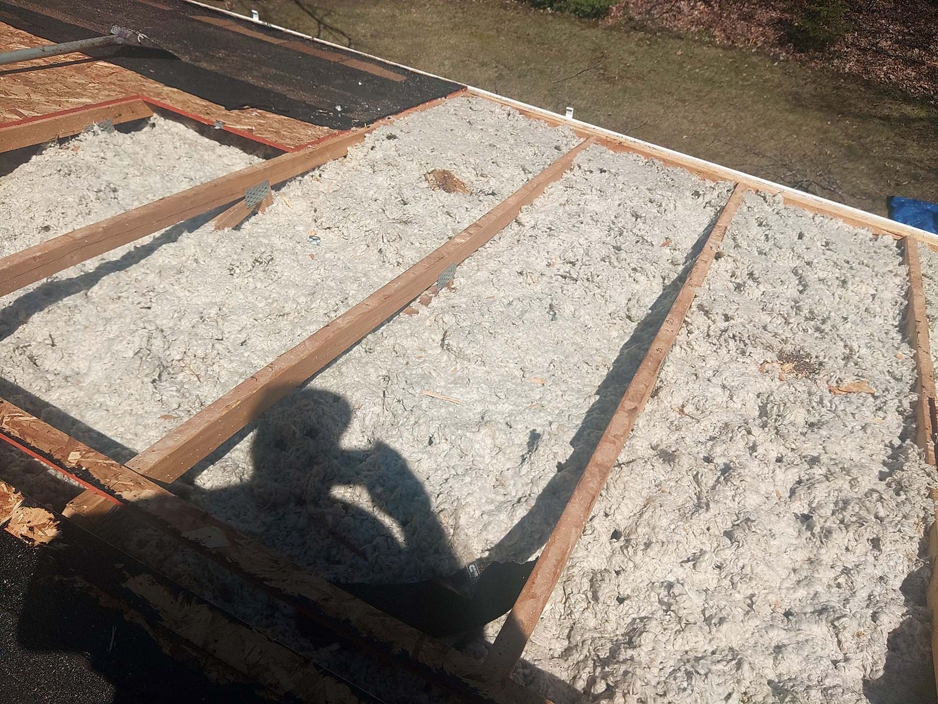 Wooden roof framework filled with light-colored insulation; a shadow of a person is cast over the scene.