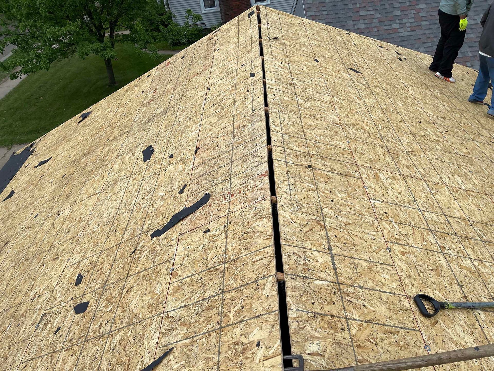 New roof under construction: OSB panels installed, central ridge gap, people standing at edge.