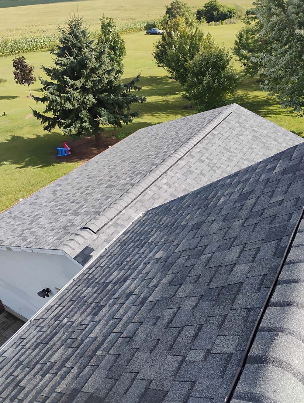 Overhead view of a gray asphalt shingle roof on a house, with a green yard and trees in the background.