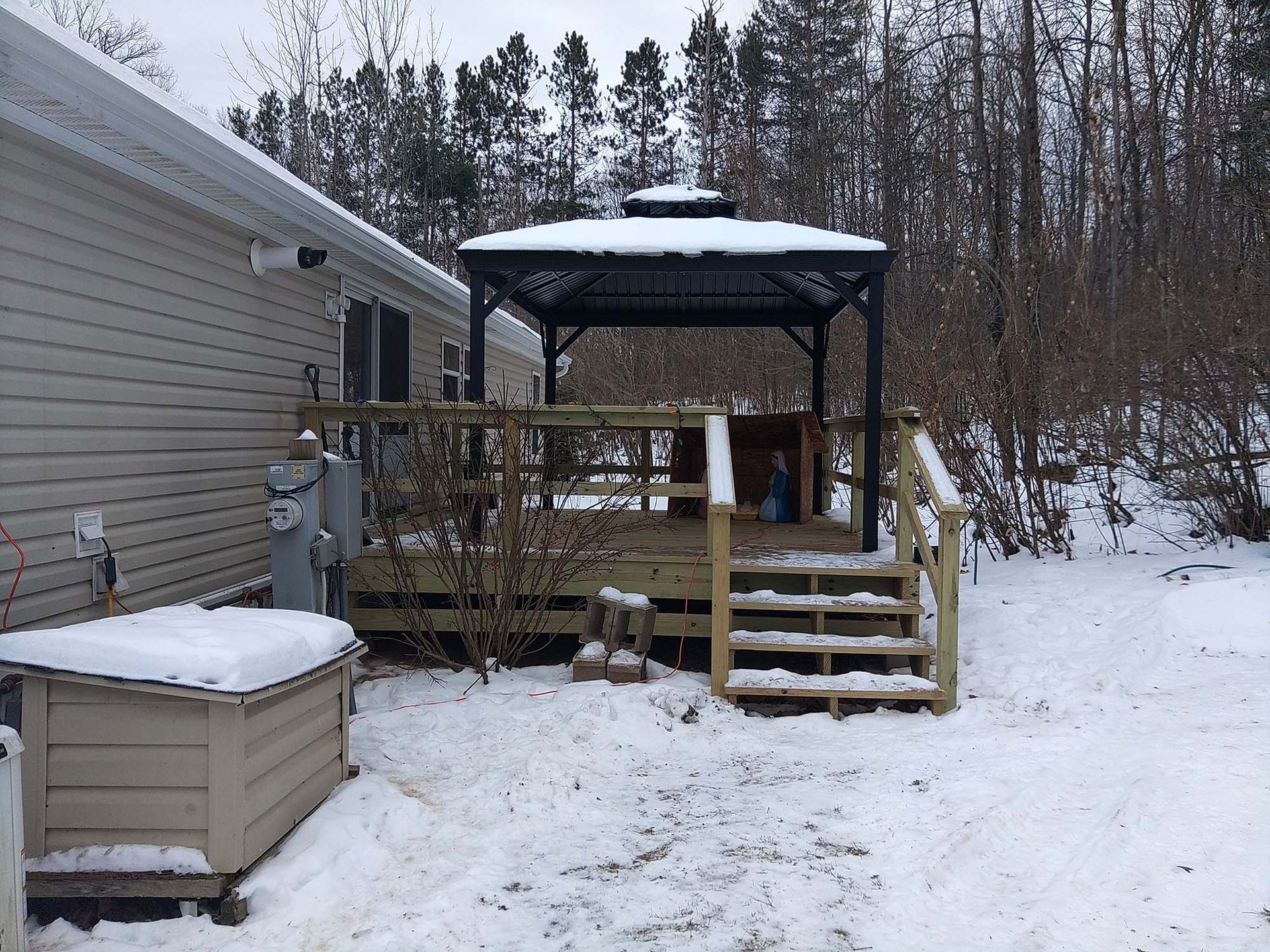 Snow-covered backyard deck with gazebo, steps, and house siding.