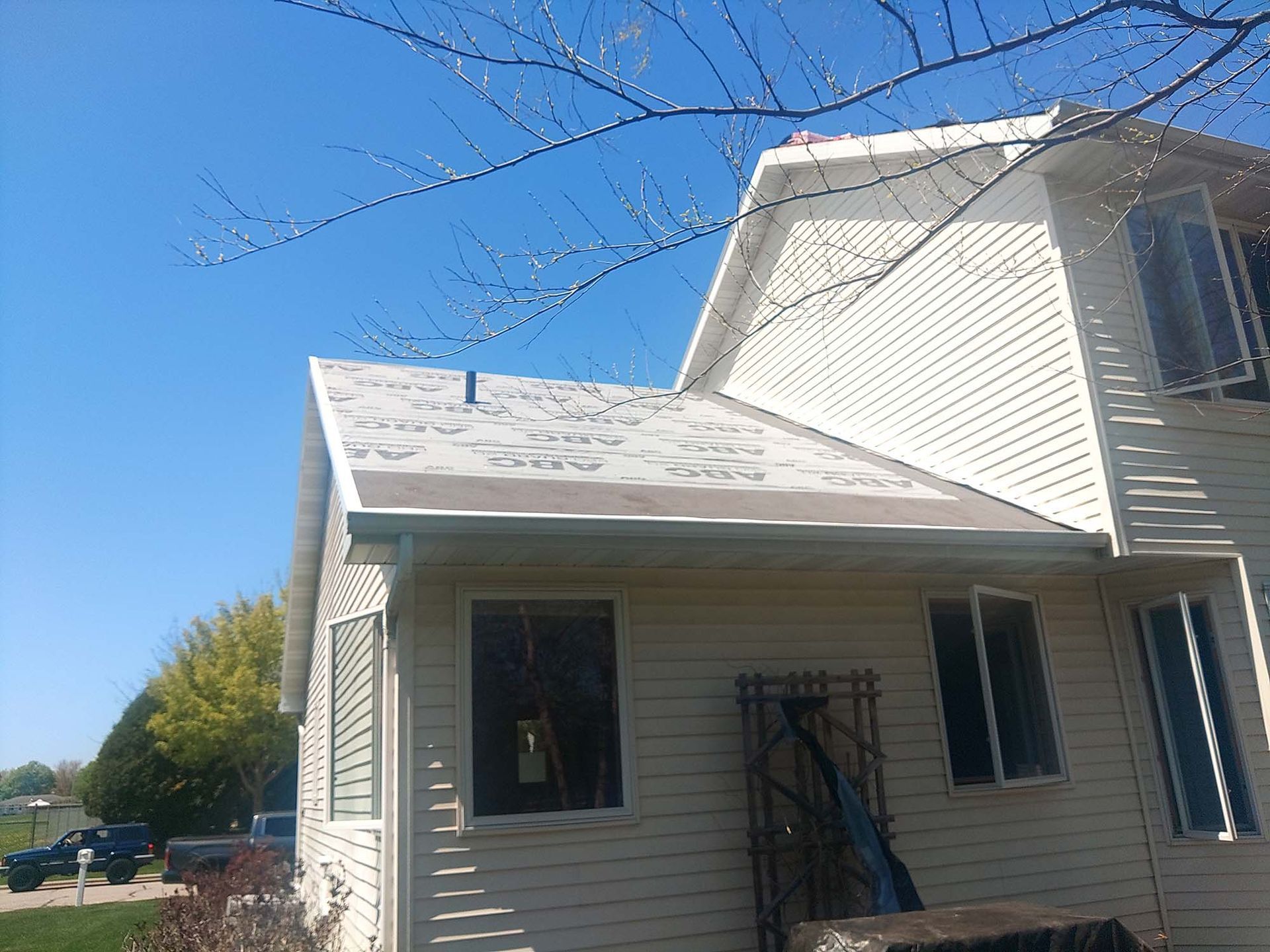 Two-story house with weathered roof under a bright blue sky.