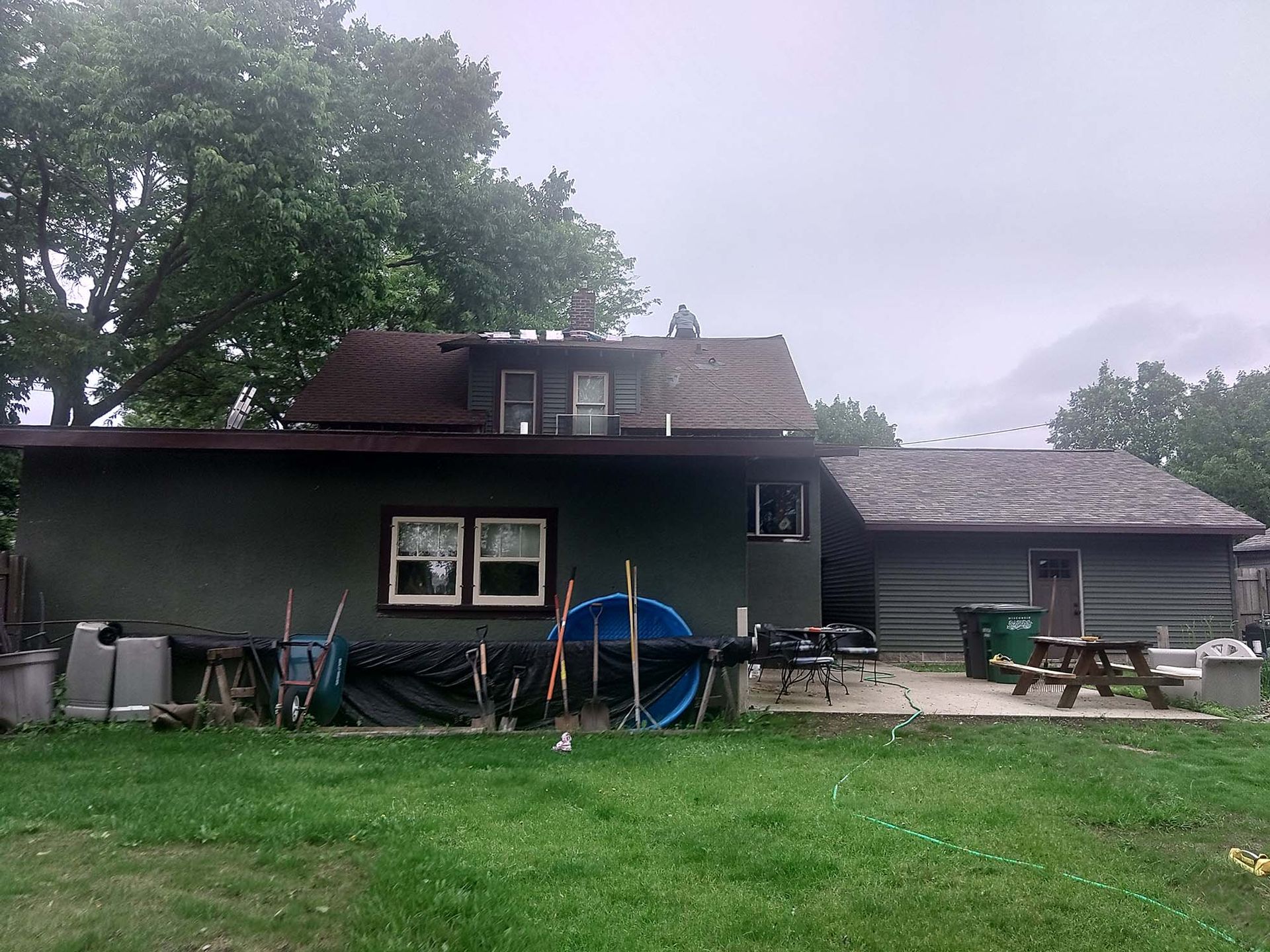 Back view of a house with a green lawn and backyard items under an overcast sky.