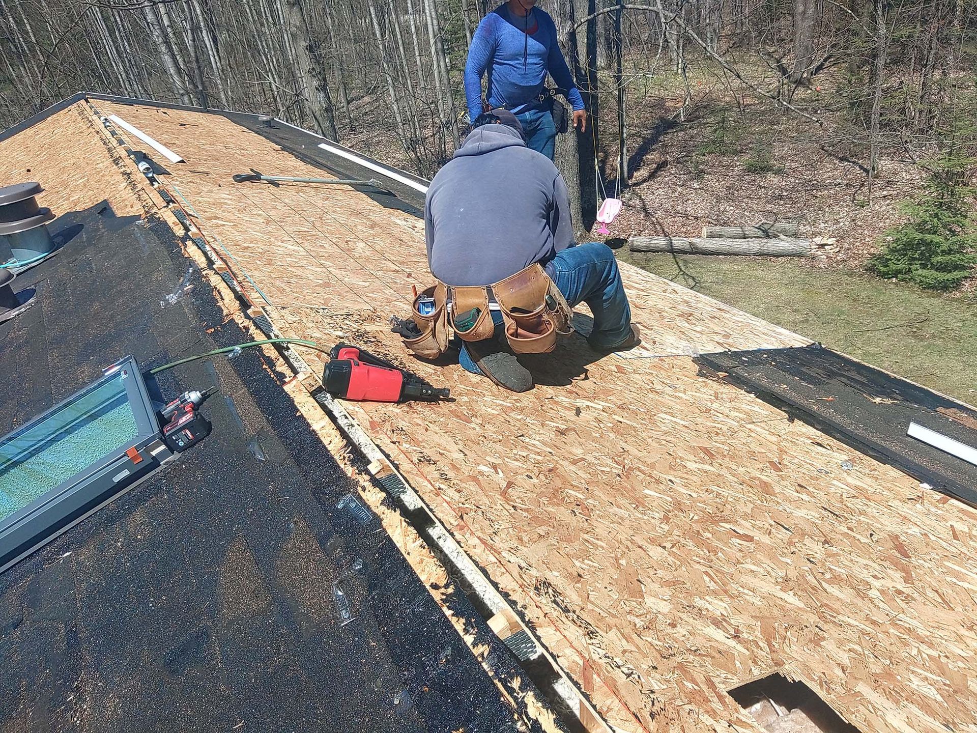 Two roofers installing shingles on a partially shingled roof. One kneels, the other stands nearby.