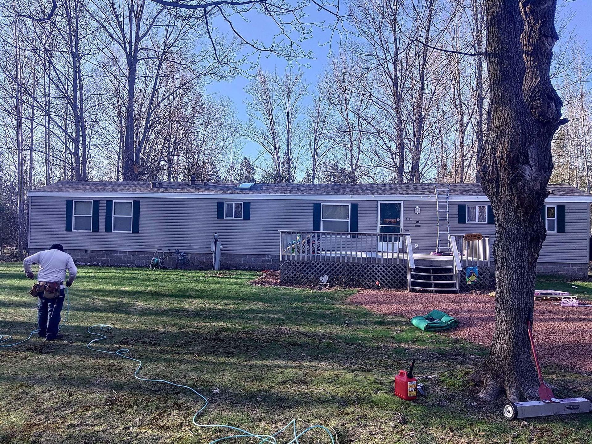 Mobile home with gray siding, a small deck, and a person in a yard with trees in the background.