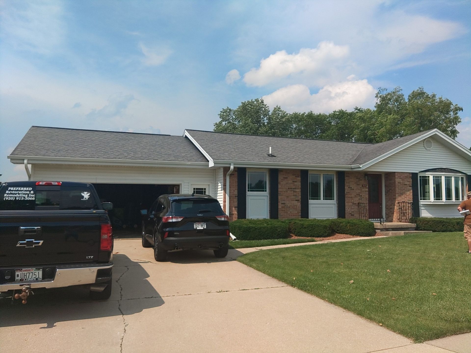 Ranch-style house with gray roof and attached garage; vehicles in driveway, green lawn.