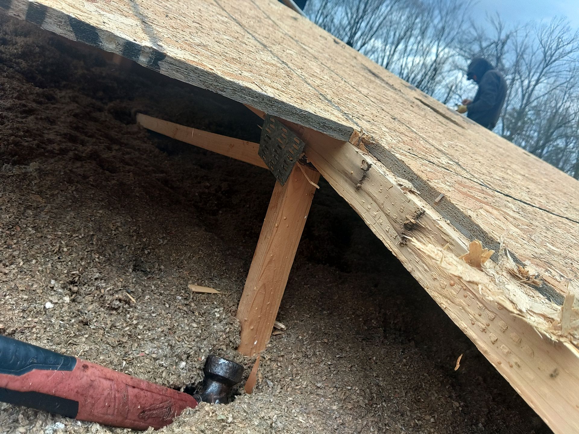 Roof repair: Hammering nails into wooden supports on a roof. A person is in the background.