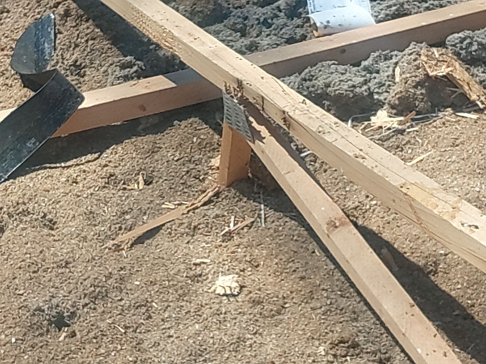 Wooden beams with metal brackets on a surface covered in brown insulation and debris.