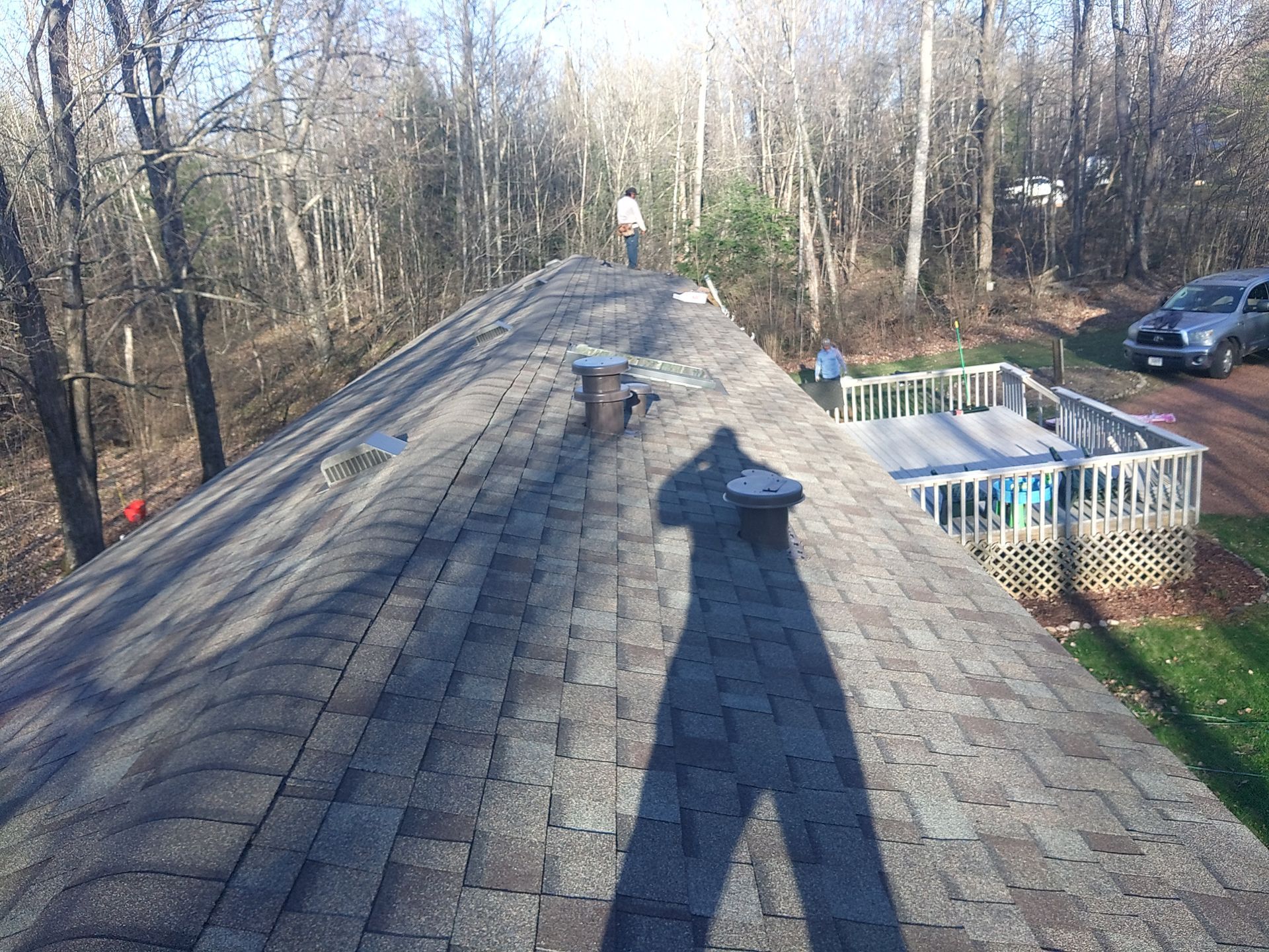 Overhead view of a roof with vent pipes, shadow of a person, and a deck with a pool.