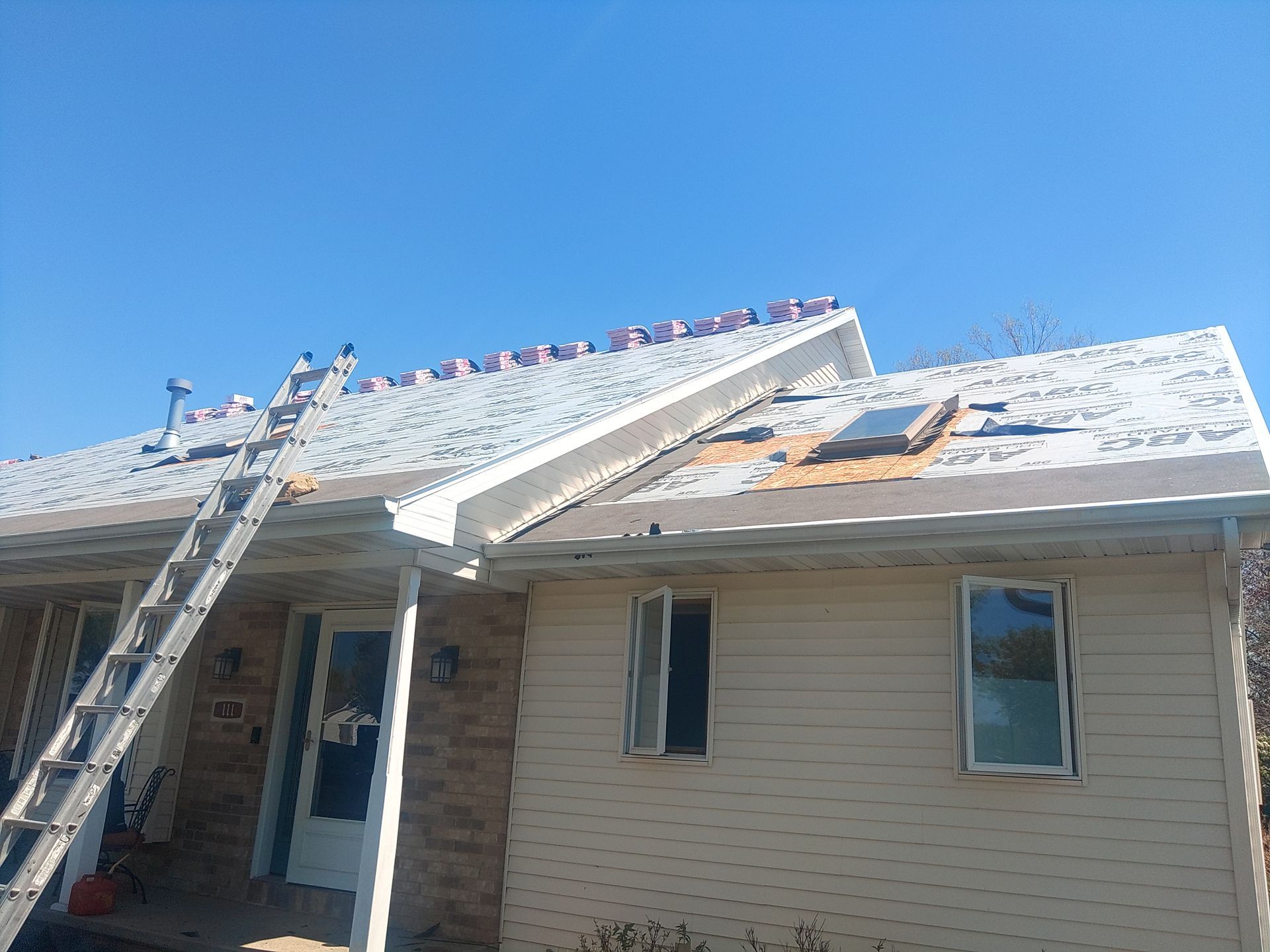 Roof being repaired on a beige house, ladder, blue sky.