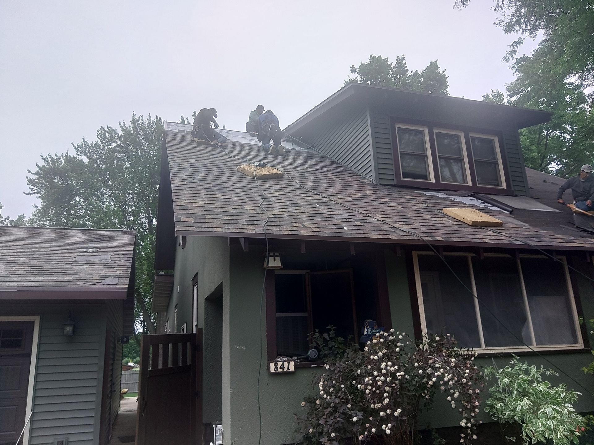 Workers removing old shingles from a house roof on a cloudy day.
