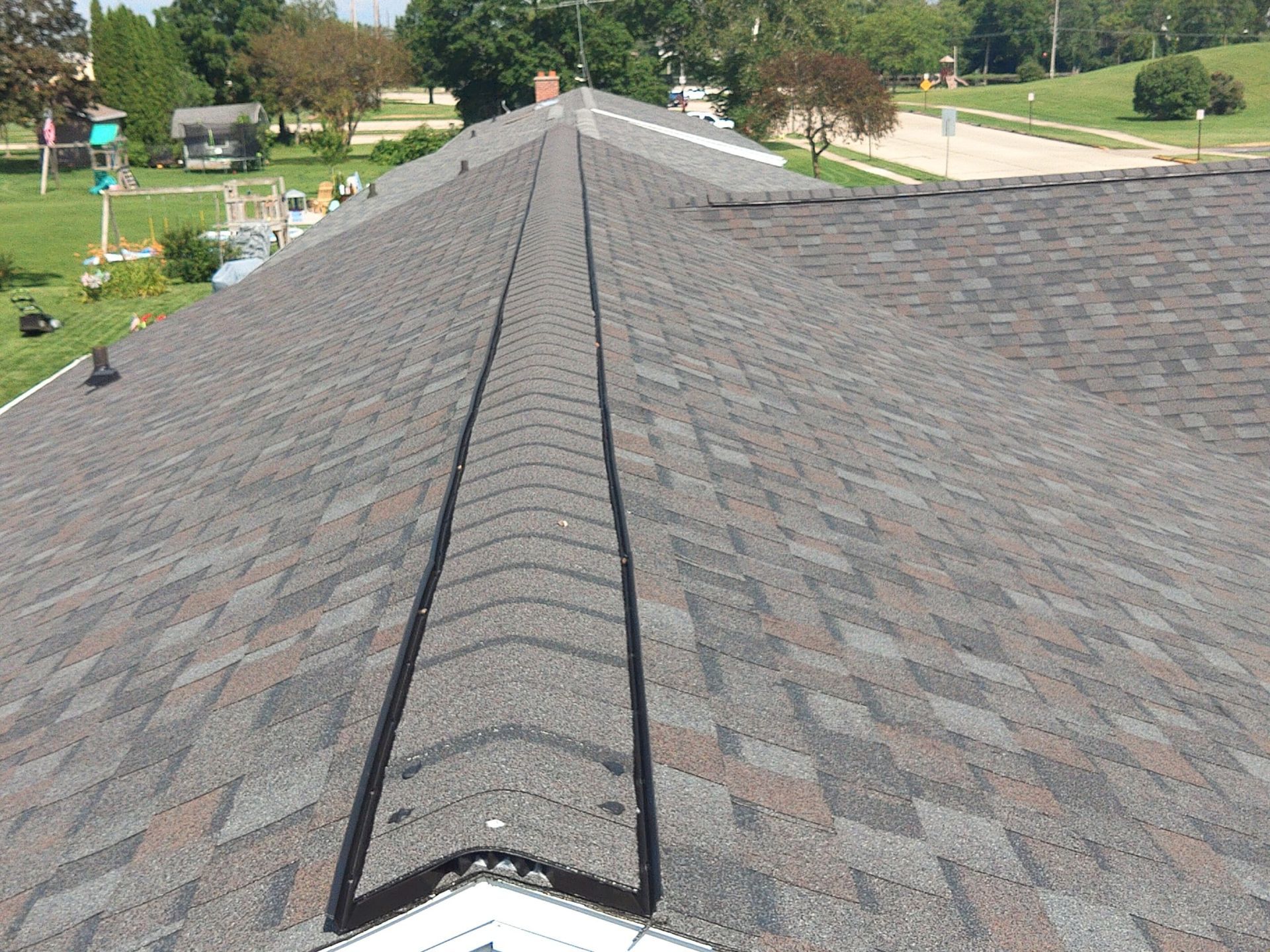 Newly shingled roof with a dark brown, gray, and red color scheme and a metal valley.