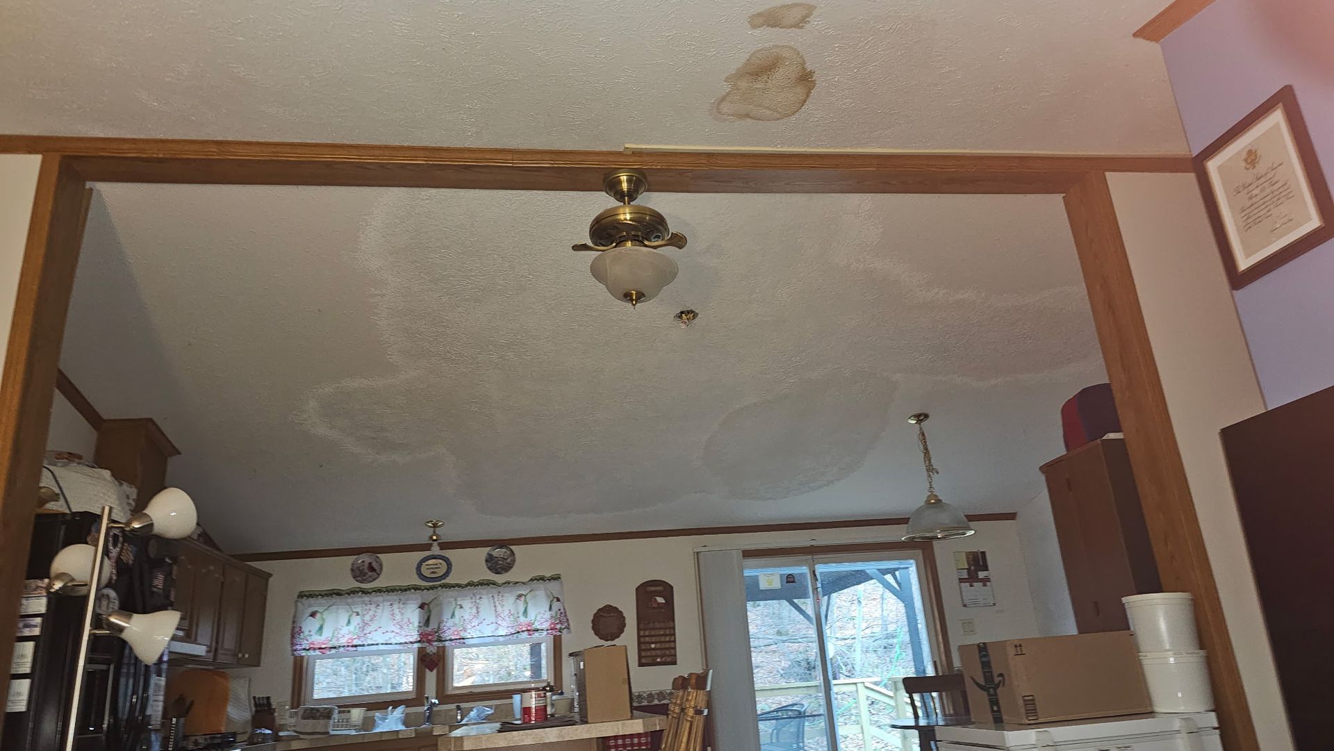 A ceiling with significant water damage, with brown support beams and a ceiling fan.