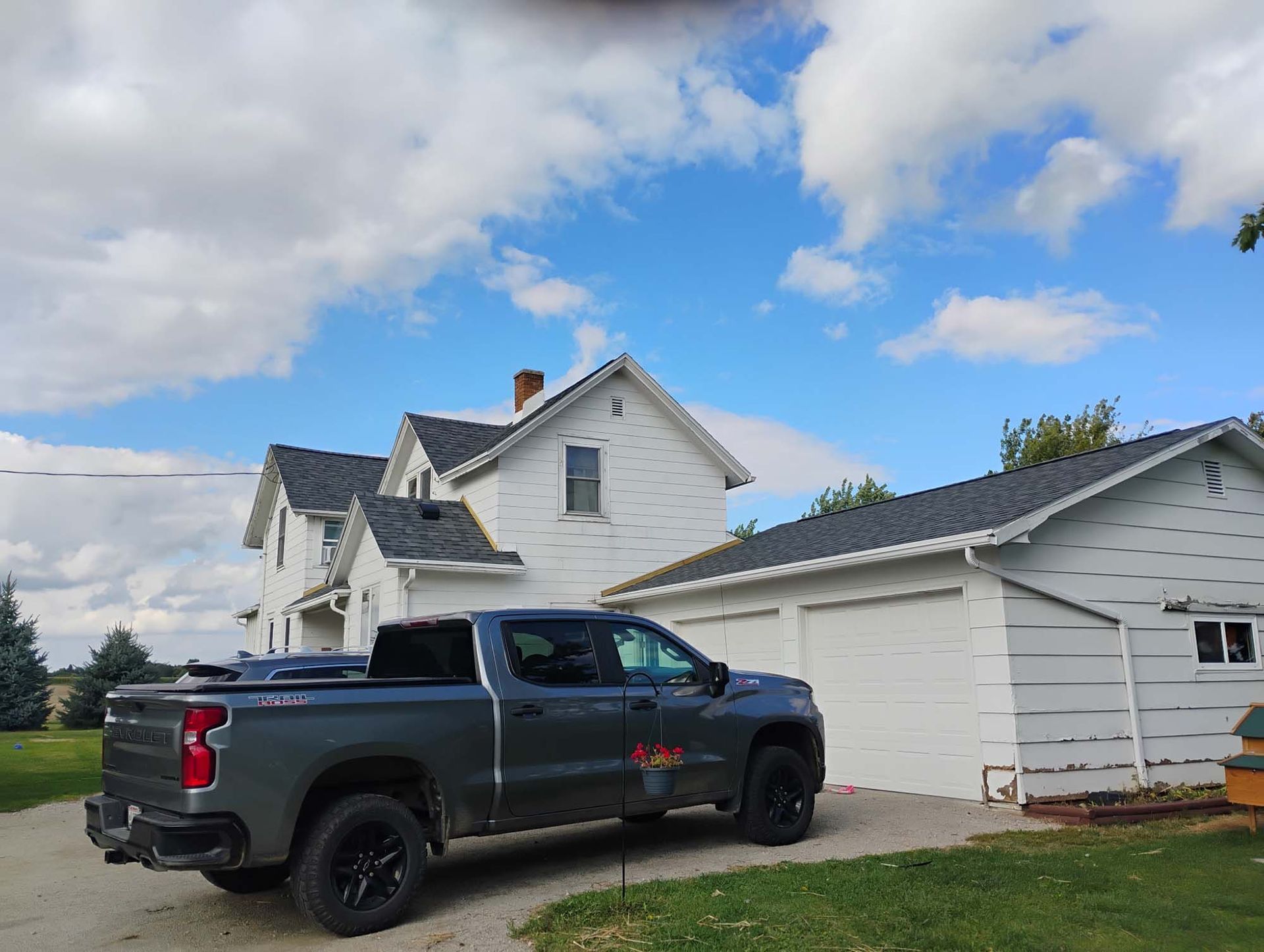 Gray truck parked in front of a white house and garage under a cloudy blue sky.