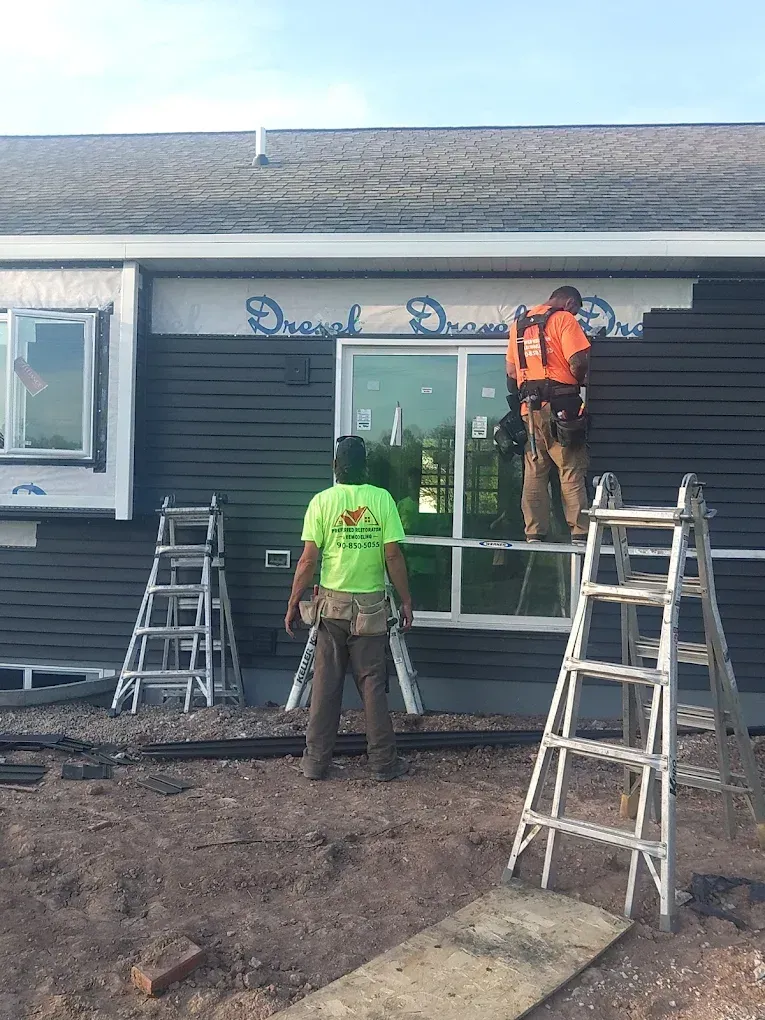 Three construction workers installing siding on a house, working with ladders, tools, and a sliding door.