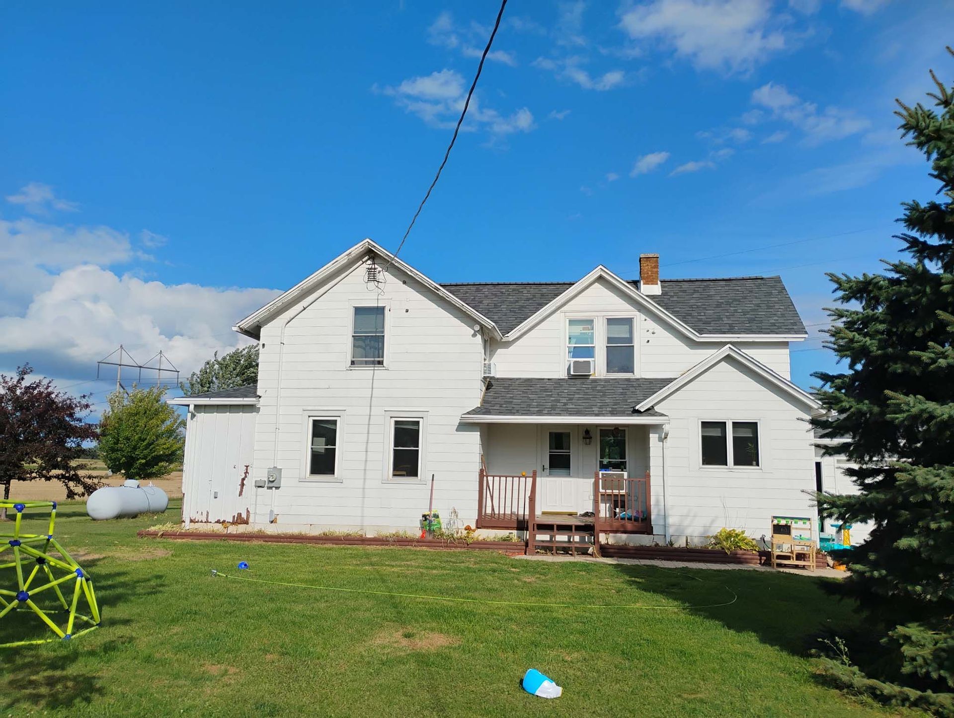 White two-story house with dark roof against a blue sky, surrounded by green grass.
