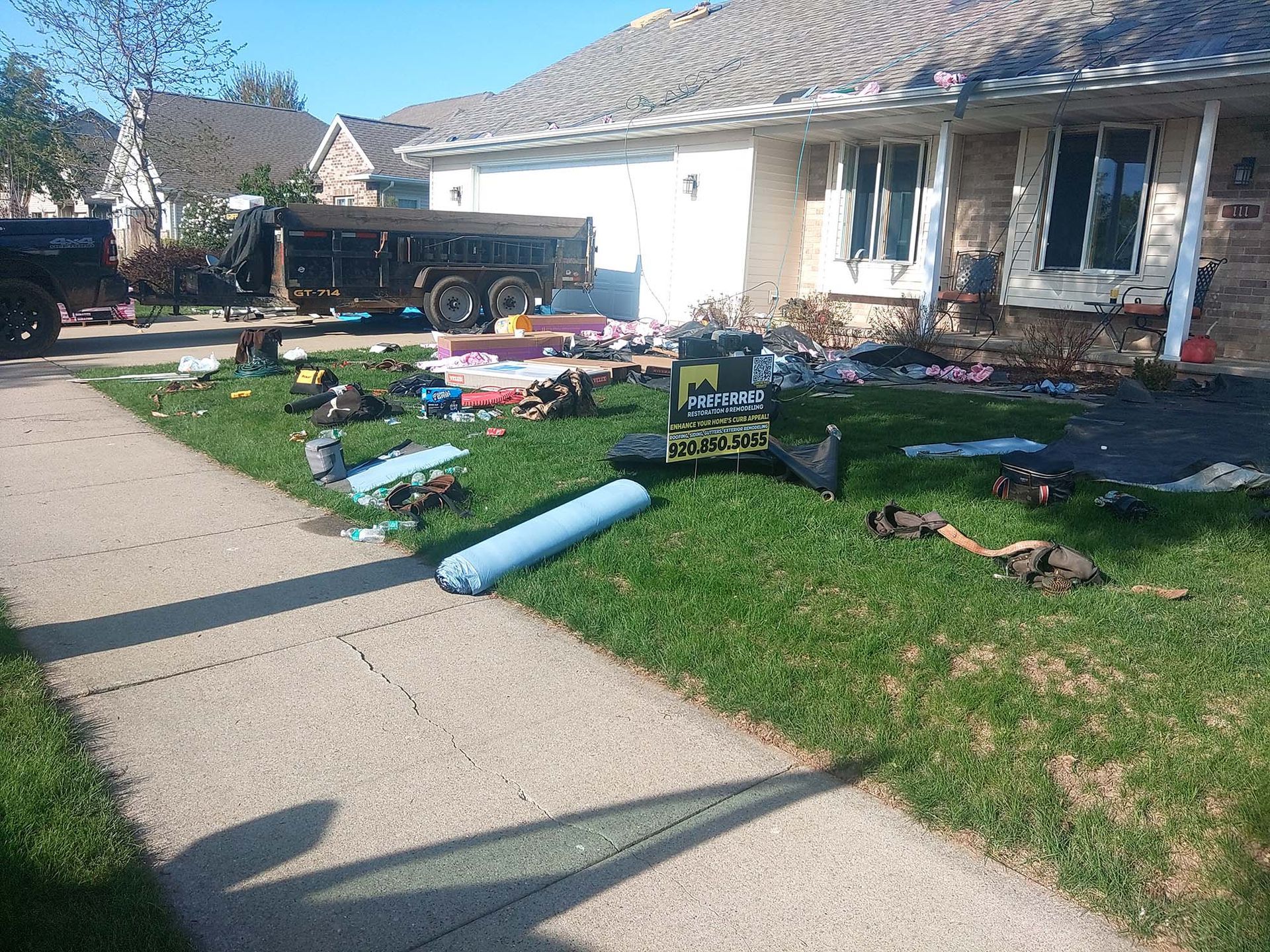 Debris scattered on a lawn in front of a house, a trailer in the background.