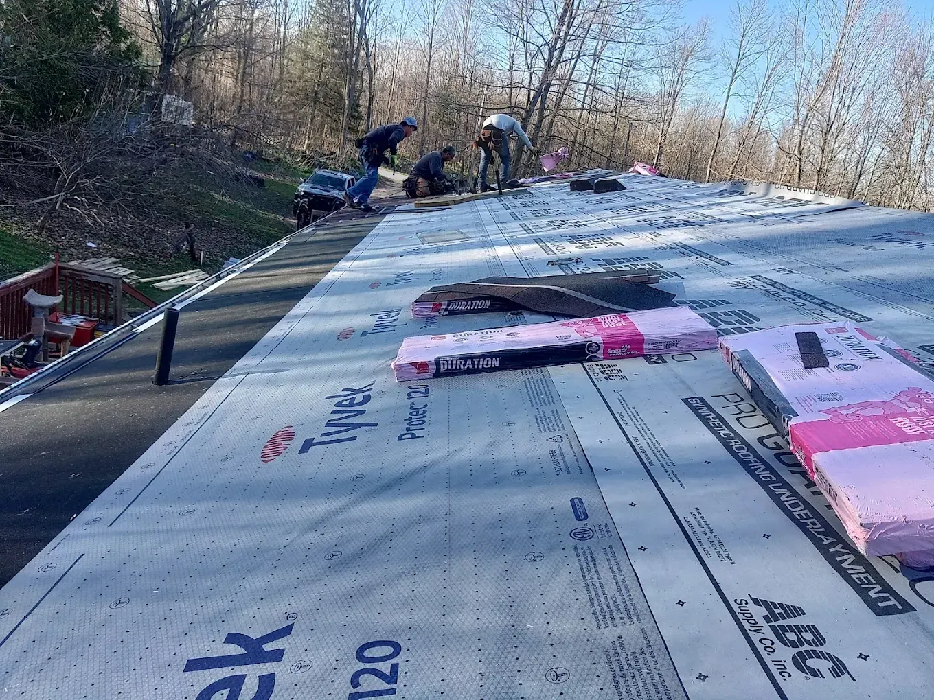 Roofers installing roofing material on a house, with Tyvek and pink insulation visible.