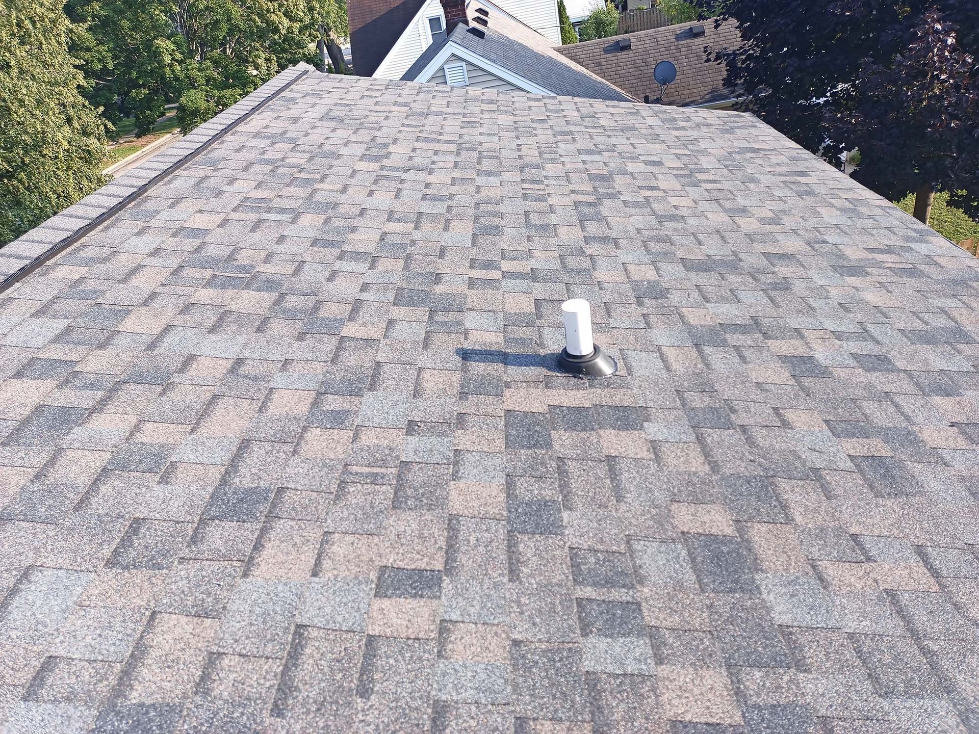 Overhead view of a roof with brown and gray shingles. A white vent pipe protrudes.