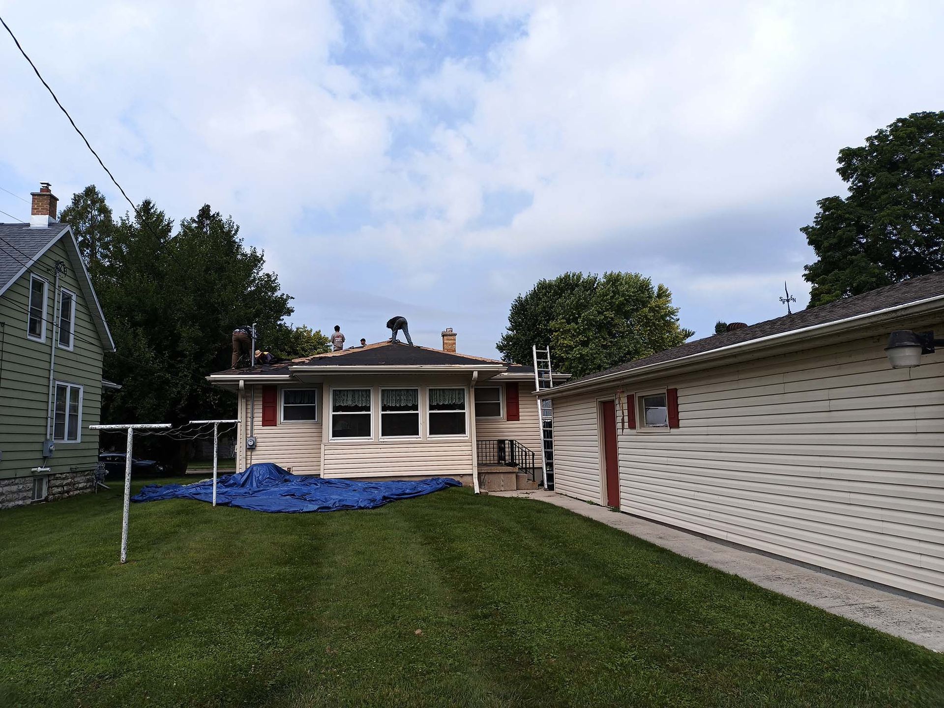 Backyard view with houses, a garage, and green grass. A blue tarp sits on the ground. Overcast sky.