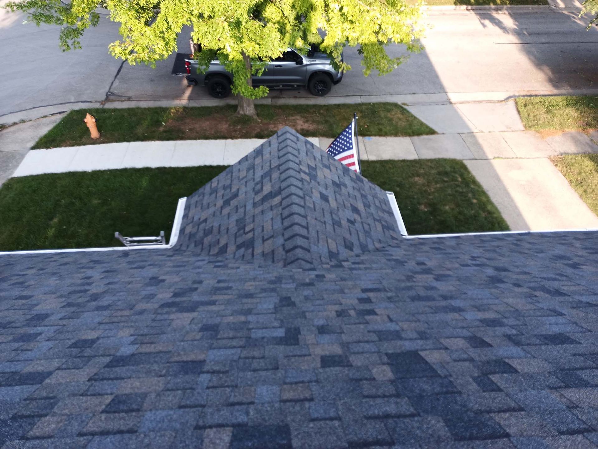 Overhead view of a house roof with dark gray shingles, American flag, and a green lawn.
