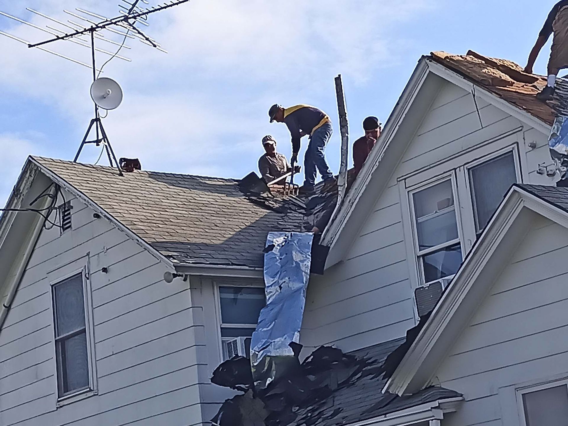 Roofers working on a residential roof, some visible from waist up, cloudy sky.