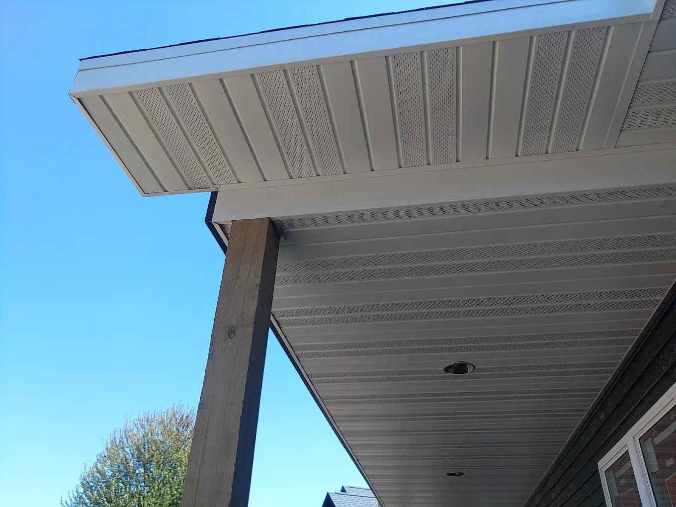 Exterior view of a house with white soffit, brown wooden post, and clear blue sky.