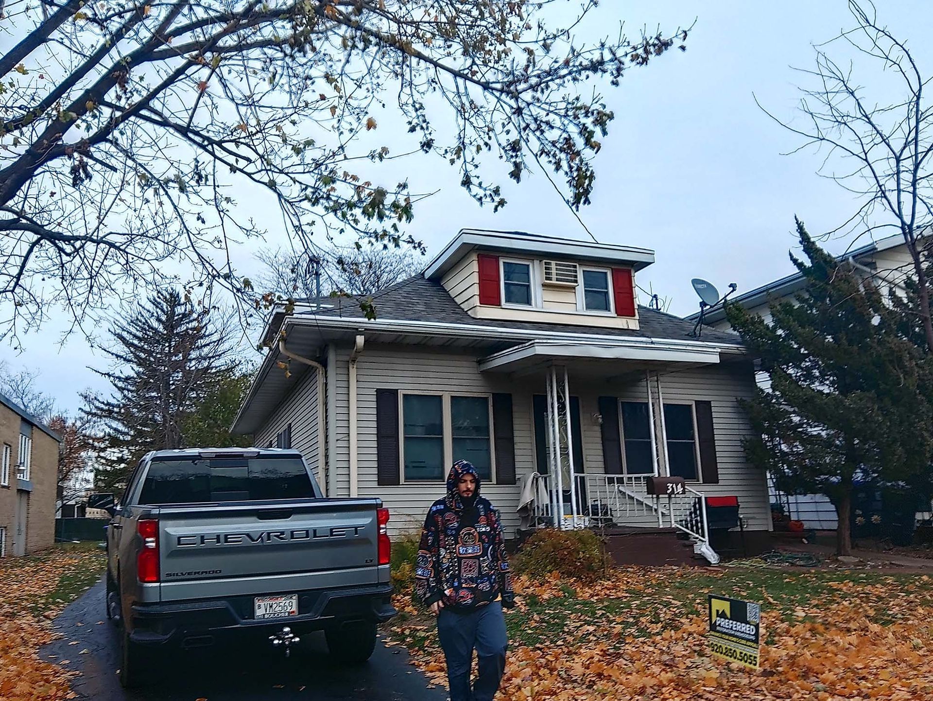Man walks towards a house with a pickup truck in the driveway, leaves on the ground.