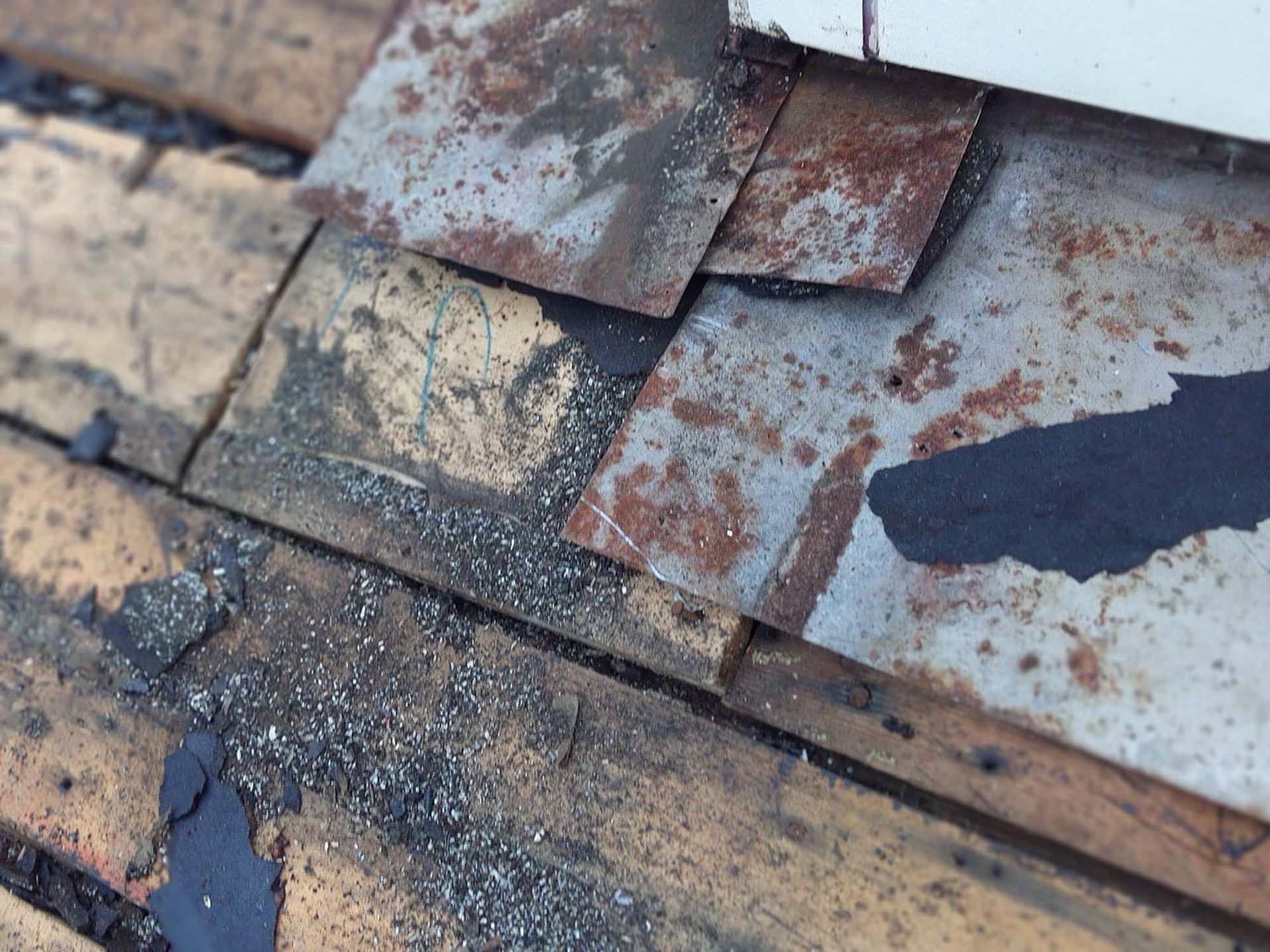 Damaged roof shingles: corroded metal and deteriorated asphalt on wooden planks.