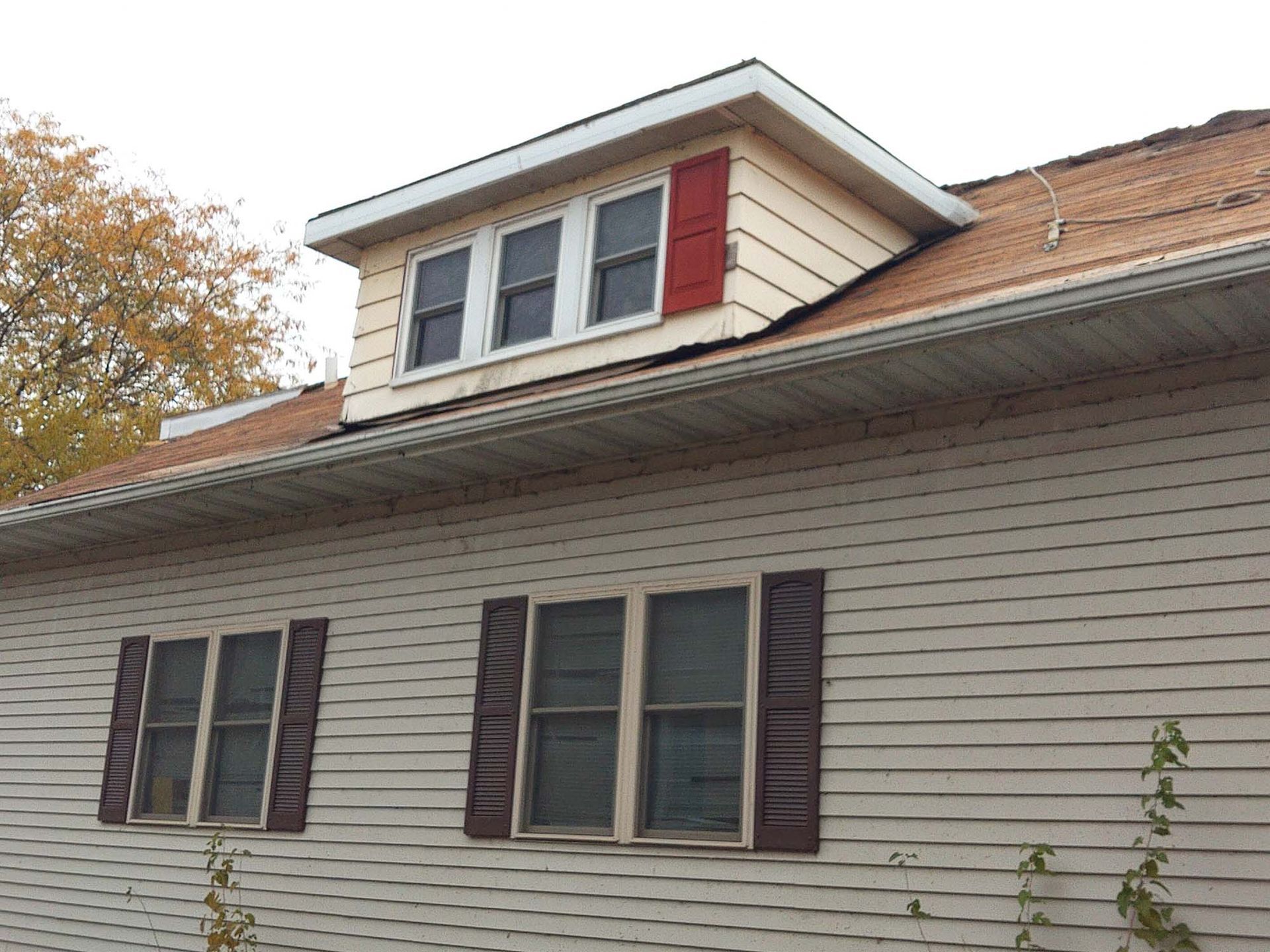 Tan house with a dormer and red shutters, set against a cloudy sky.