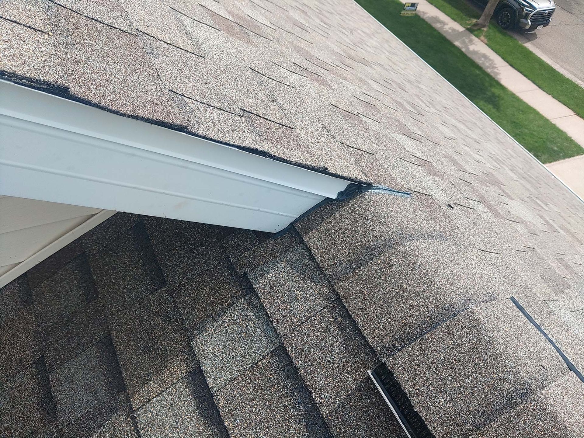 Close-up view of a roof with gray shingles and a white eave, angled toward a street and grass.