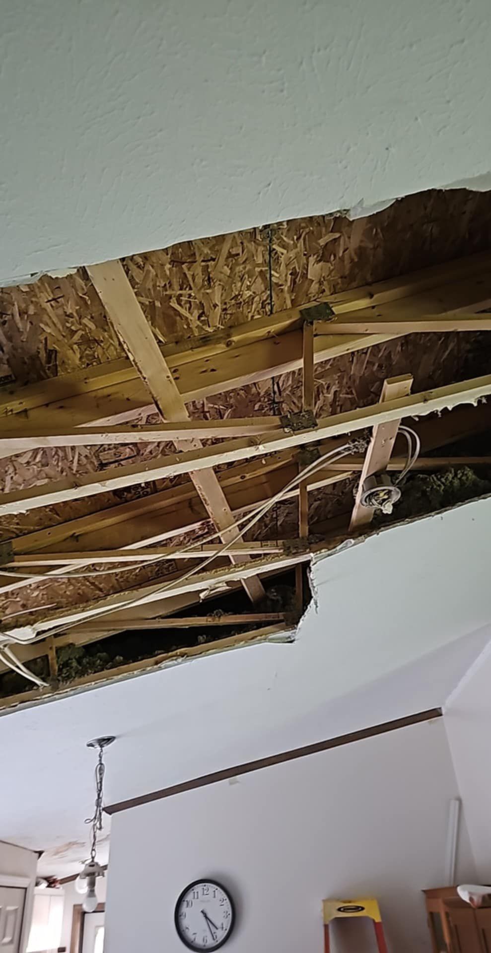 Damaged ceiling reveals beams, wires, and insulation. White ceiling with a large hole, indoors.