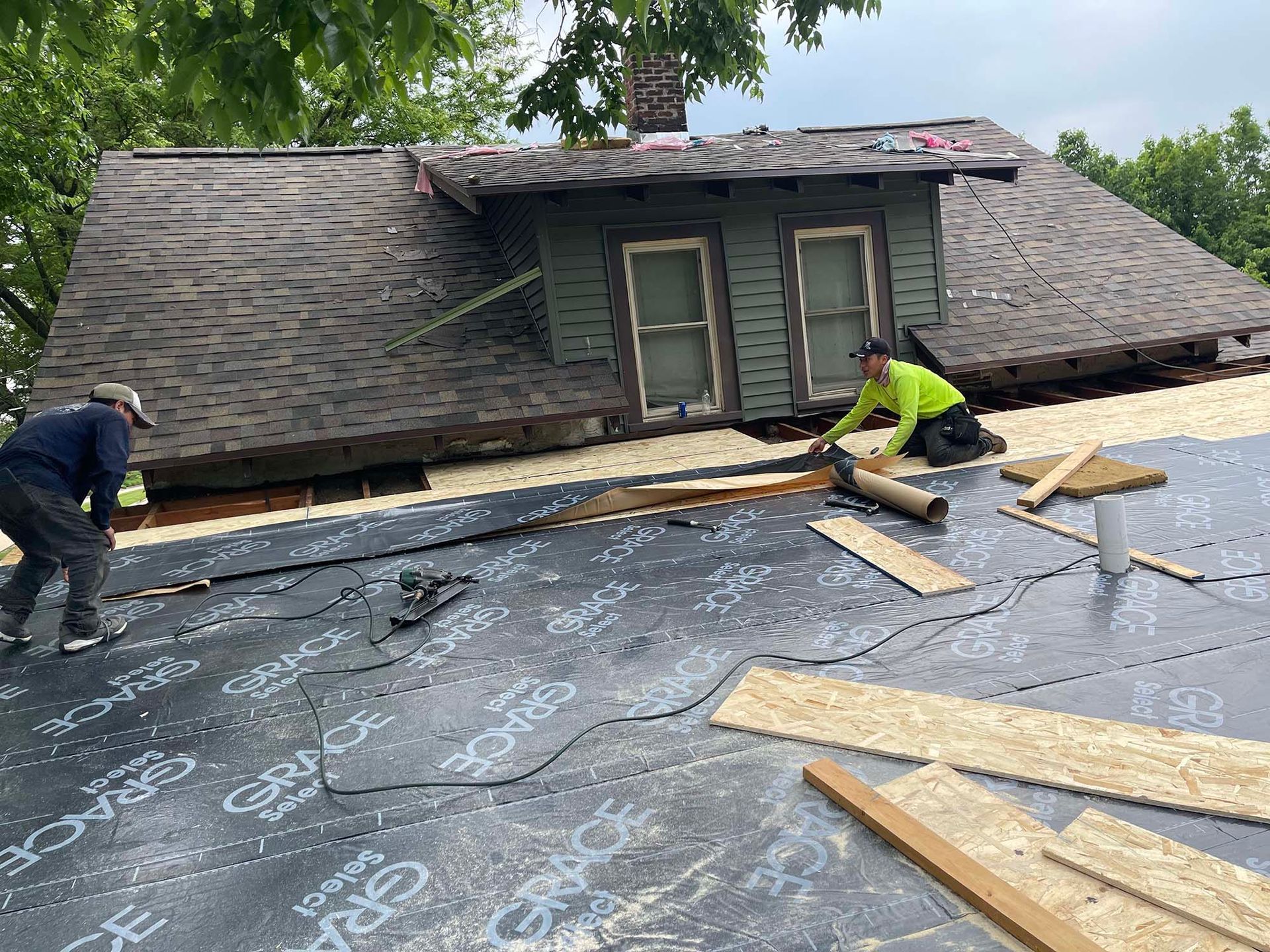 Two roofers installing roofing material on an older house. The setting is outdoors.