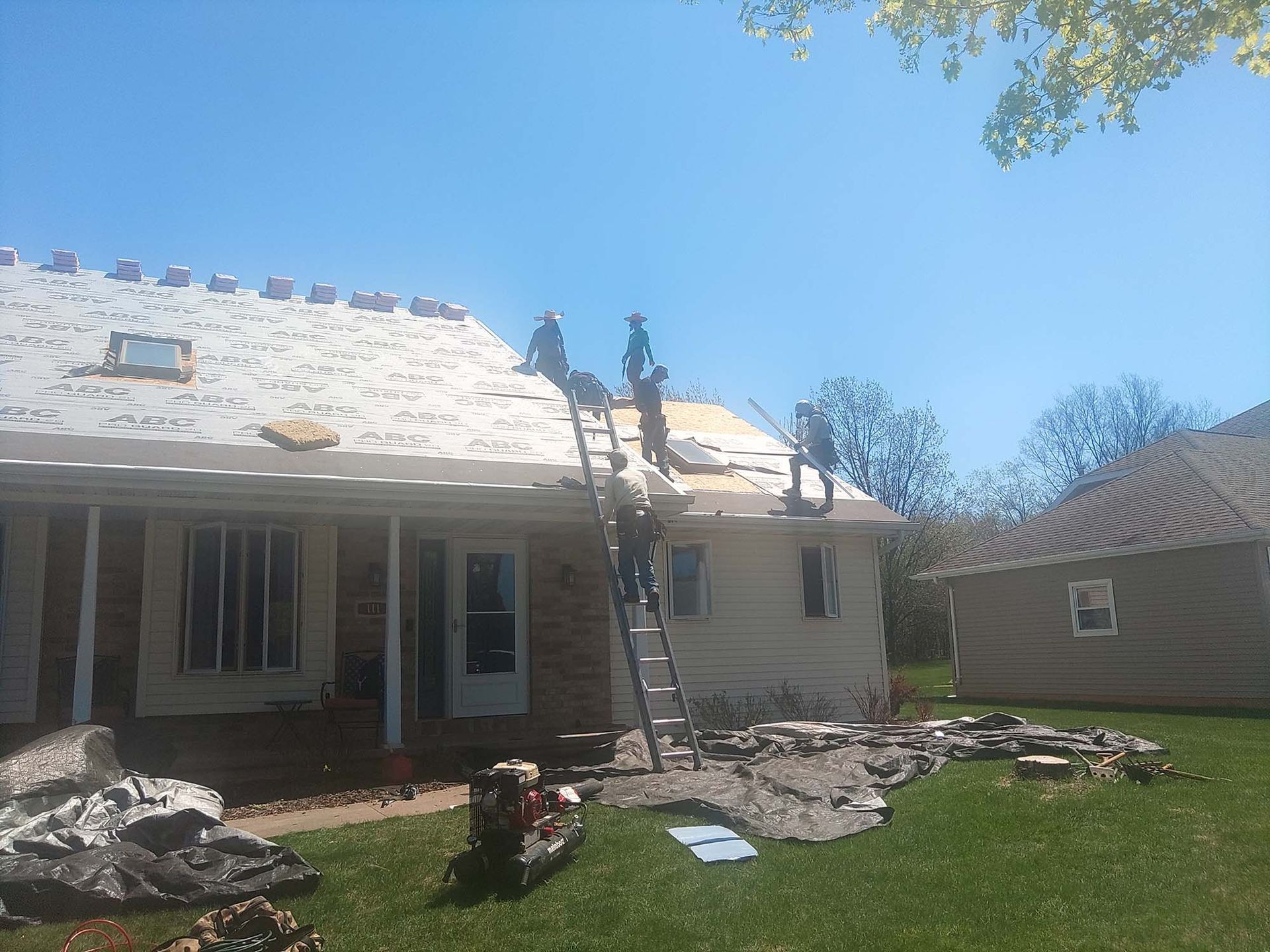 Roofers on a ladder, working on a house roof on a sunny day.