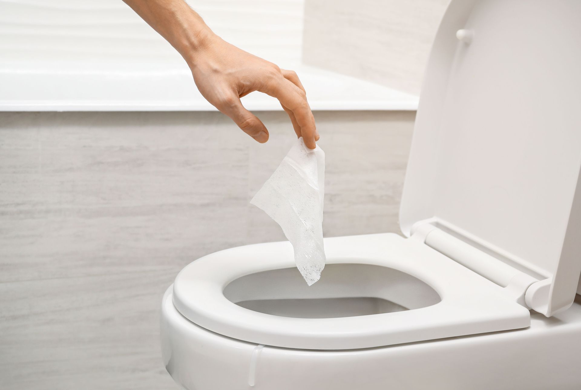 A hand dropping toilet paper into a toilet.